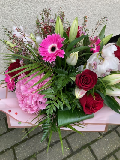 Deluxe Delight - This delicate deluxe hand tied bouquet is made using a mixture of red , pink  and white flowers. It will include roses and orchids. The design will also have soft foliage and filler flowers and be gift wrapped.